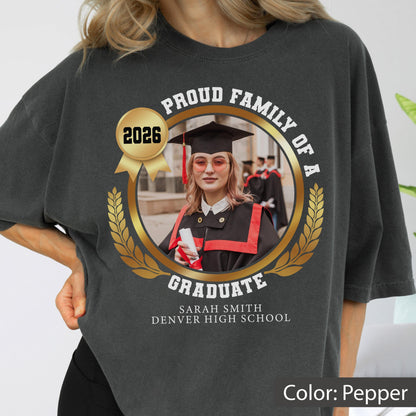 May include: Pepper-colored t-shirt with a graduation design. The design includes a photo of a graduate, the text "Proud Family of a Graduate," the year 2026, and the graduate's name and high school.