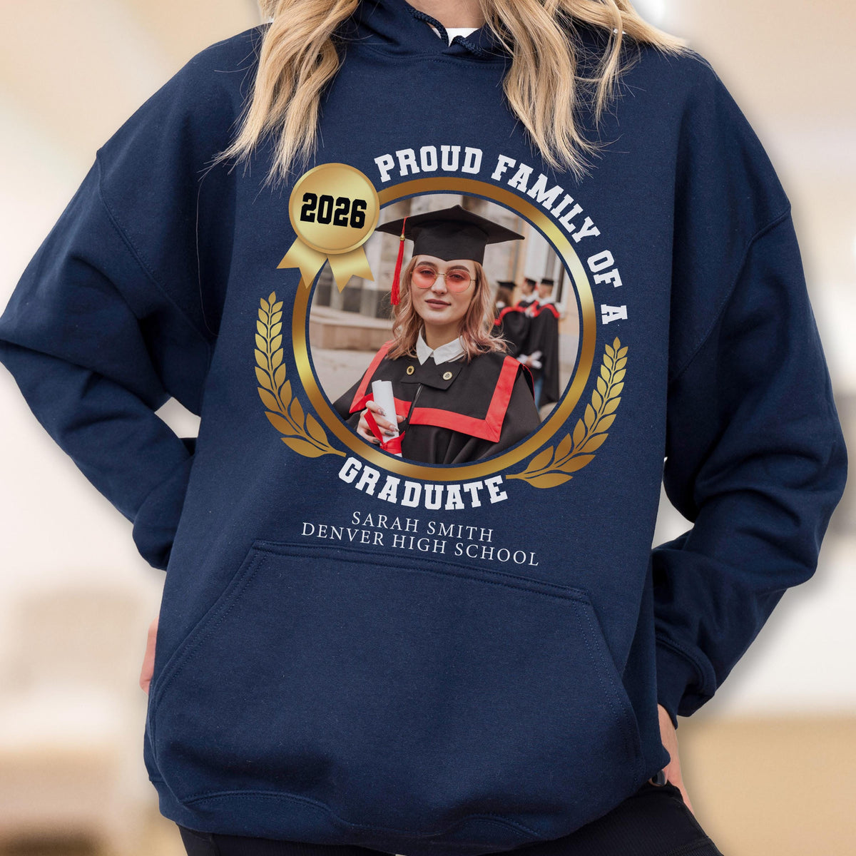 May include: Navy blue hooded sweatshirt with a gold emblem featuring a graduate's photo, the year 2026, and the text "Proud Family of a Graduate." The graduate's name and high school are also displayed. A personalized graduation gift.