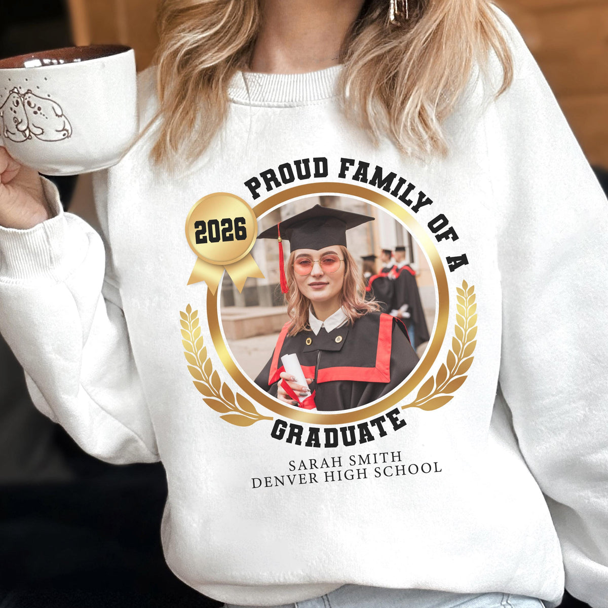 May include: White sweatshirt with a graduation-themed design. The design includes a photo of a graduate, the text "PROUD FAMILY OF A GRADUATE", the year "2026", and the graduate's name and high school. The sweatshirt is a crew neck style.