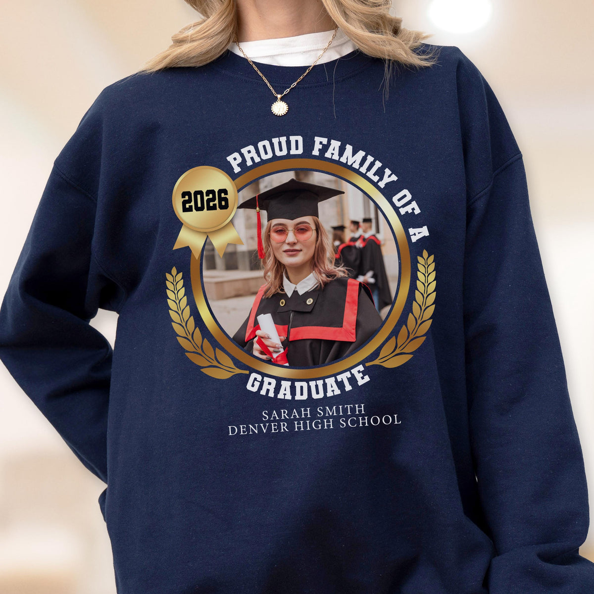 May include: Navy blue sweatshirt with a gold emblem featuring a graduate's photo, the year 2026, and the text "Proud Family of a Graduate." The graduate's name and high school are also displayed.