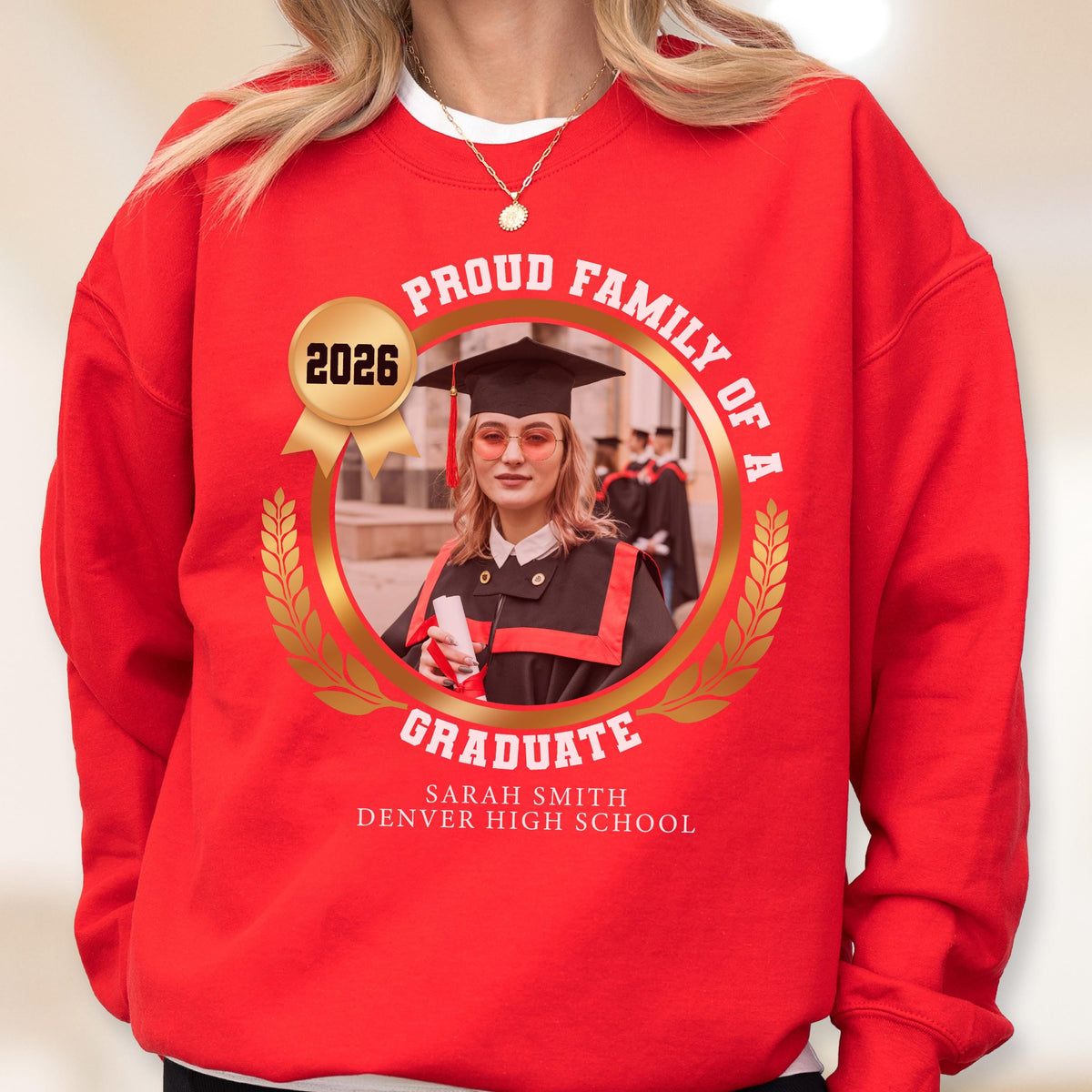 May include: Red sweatshirt with a gold emblem featuring a graduate's photo, the text "PROUD FAMILY OF A GRADUATE," and the year 2026. The graduate is wearing a cap and gown. The text "SARAH SMITH DENVER HIGH SCHOOL" is also included.