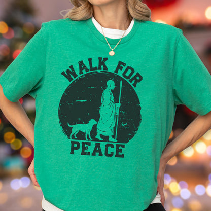 May include: A bright green short-sleeved t-shirt featuring a black graphic of a person in robes walking with a staff alongside a dog. The text "WALK FOR PEACE" is printed in black capital letters around the circular graphic design.