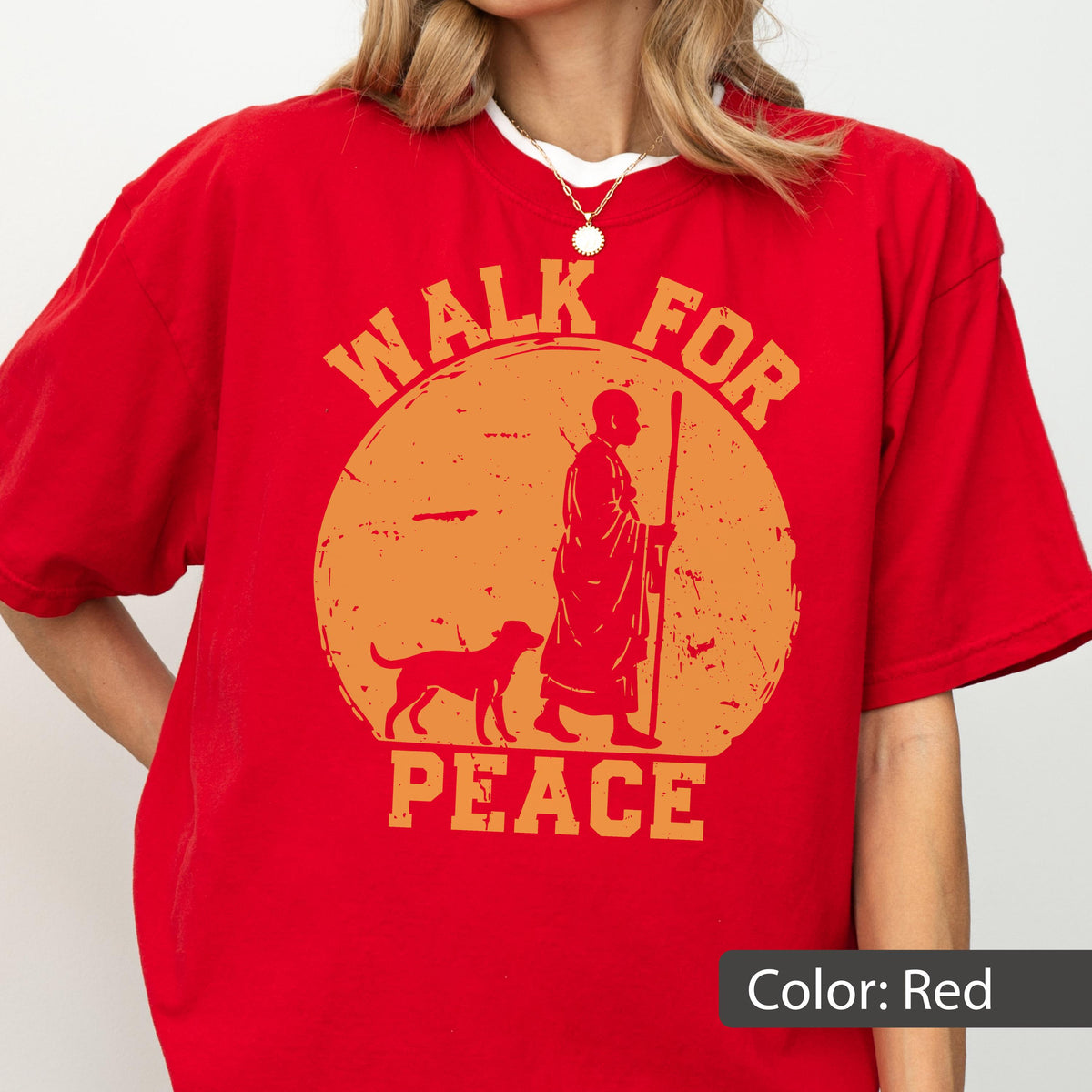 May include: Red t-shirt with an orange graphic featuring a person with a dog and the words "WALK FOR PEACE". The design is inside a circle. The shirt is a solid red color.
