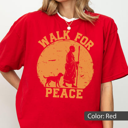 May include: Red t-shirt with an orange graphic featuring a person with a dog and the words "WALK FOR PEACE". The design is inside a circle. The shirt is a solid red color.