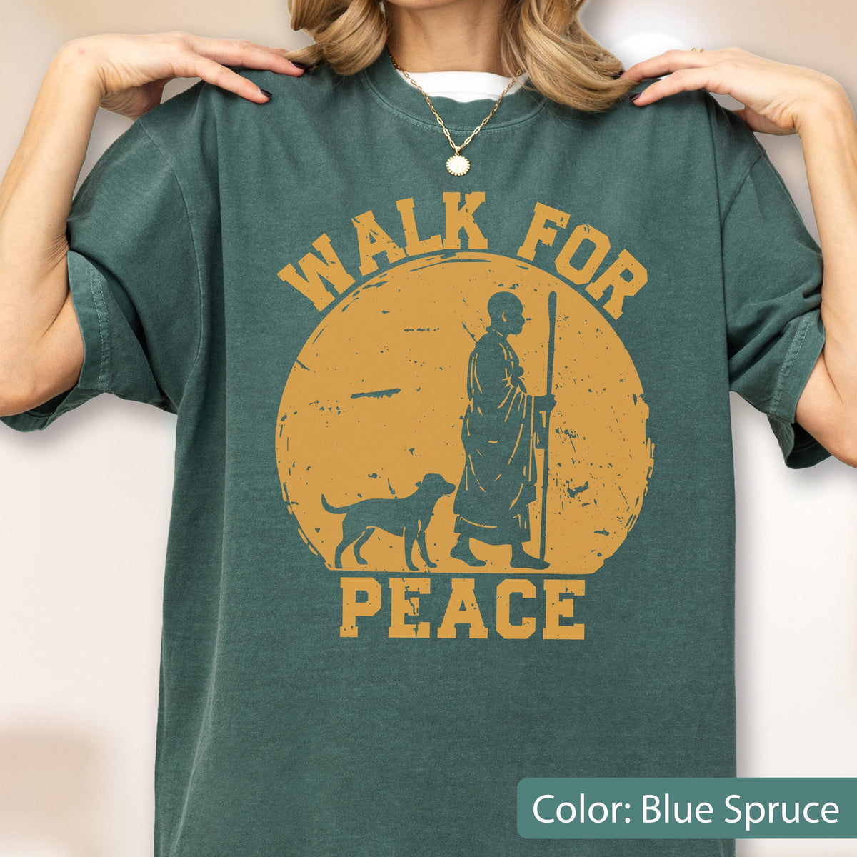 May include: Blue spruce t-shirt with a distressed graphic. The design features a figure with a dog walking in front of a yellow sun, with the words "WALK FOR PEACE" in a circular layout.
