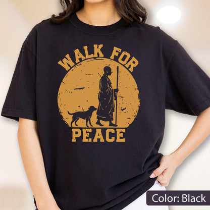 May include: Black t-shirt with a distressed gold graphic of a person walking with a dog and staff in front of a sun. The text "WALK FOR PEACE" is arched above and below the image.
