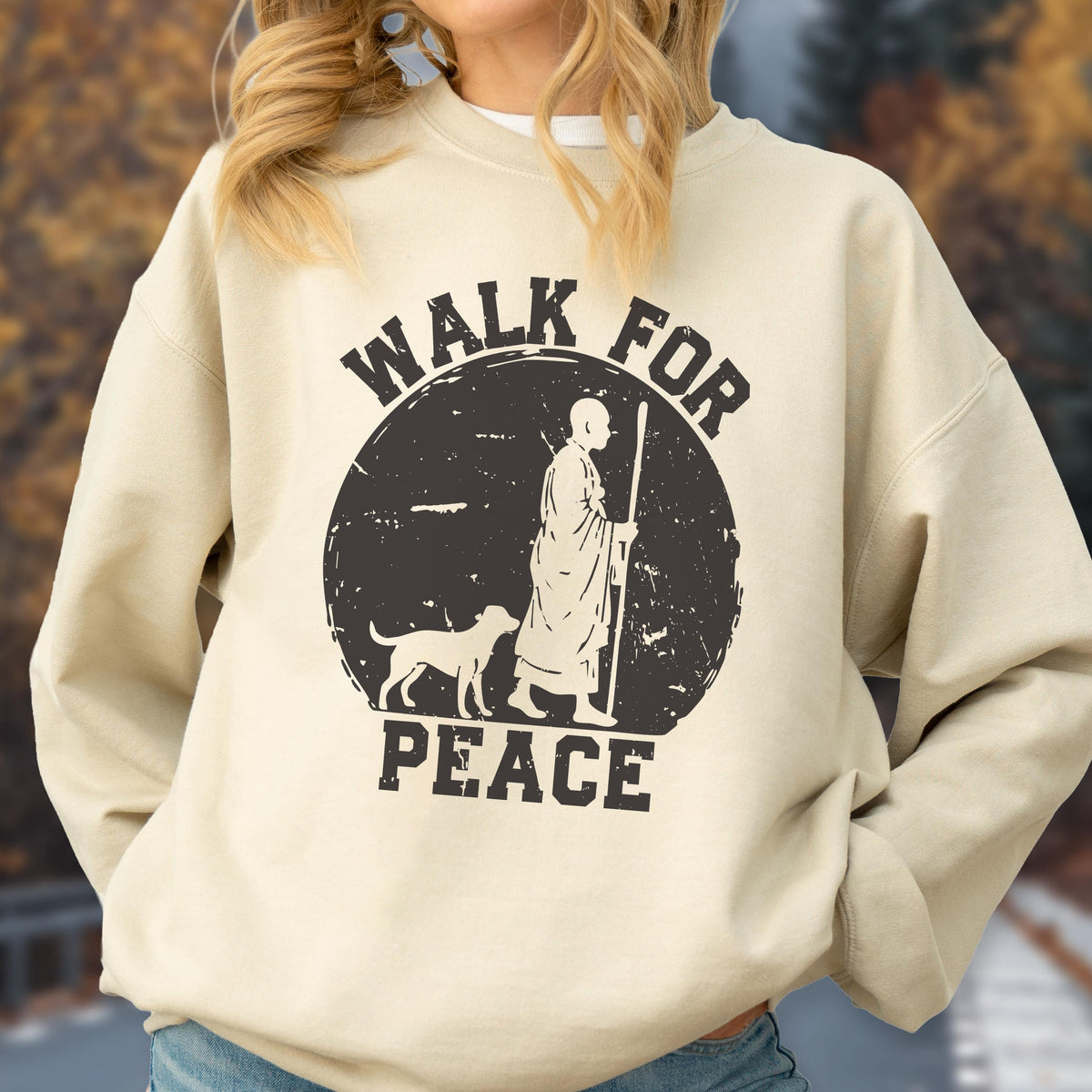 May include: Beige sweatshirt with a black graphic. The graphic features a figure with a dog and the words "WALK FOR PEACE" in a distressed font. The sweatshirt is a neutral color, suitable for casual wear.