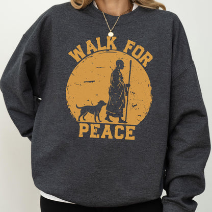 May include: Dark gray sweatshirt with a distressed orange graphic. The graphic features a person with a staff and a dog walking in front of a yellow sun with the words "WALK FOR PEACE". The sweatshirt has a crew neck and long sleeves.