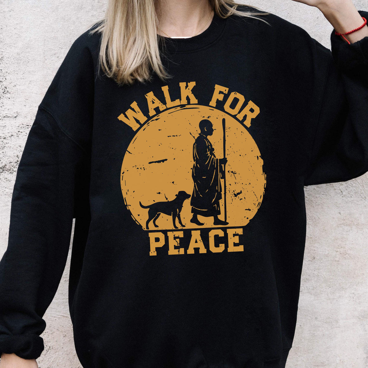 May include: Black sweatshirt with a golden-yellow graphic. The graphic features a figure with a staff, a dog, and the words "WALK FOR PEACE" in a circular design. The sweatshirt is a crew neck style.