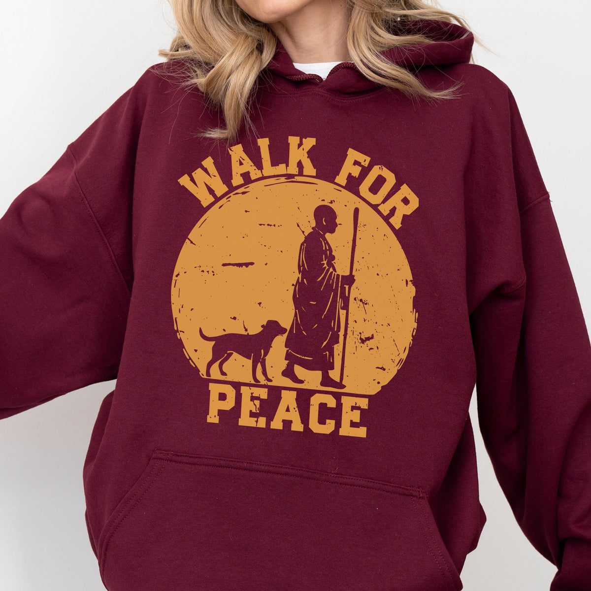 May include: Burgundy hoodie with a distressed gold graphic. The graphic features a person with a dog, holding a staff, inside a circle with the words "WALK FOR PEACE". The hoodie has a drawstring hood and a kangaroo pocket.