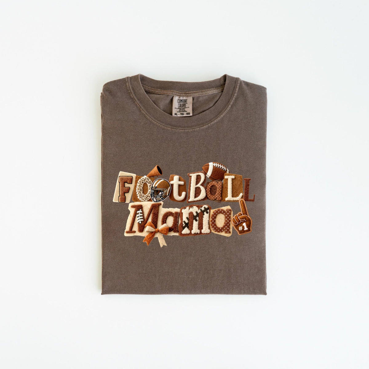 May include: A brown t-shirt with the words "Football Mama" in a decorative font. The design includes footballs, a helmet, and a foam finger. The shirt is folded neatly on a white surface.