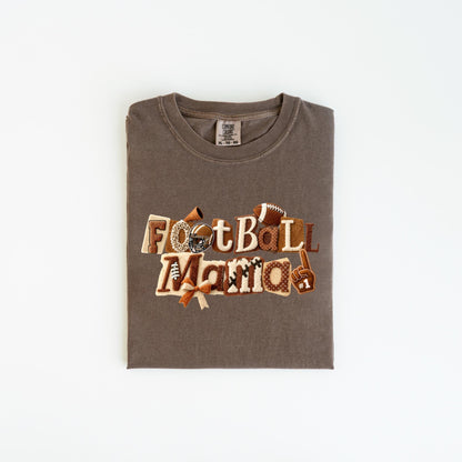 May include: A brown t-shirt with the words "Football Mama" in a decorative font. The design includes footballs, a helmet, and a foam finger. The shirt is folded neatly on a white surface.