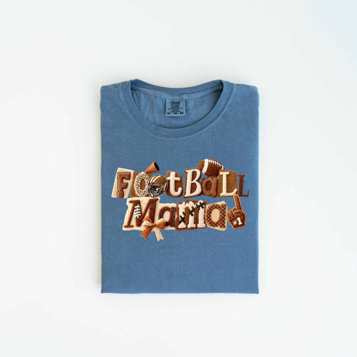 May include: A blue t-shirt with the words "Football Mama" in a decorative design. The design includes footballs, a helmet, and a foam finger. The shirt is folded and laid flat on a white surface.