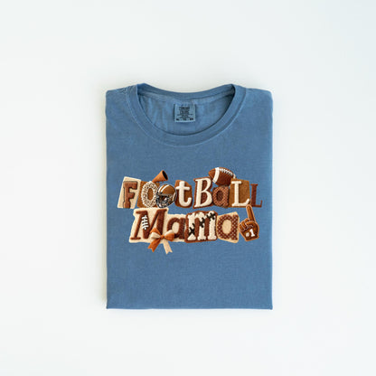 May include: A blue t-shirt with the words "Football Mama" in a decorative design. The design includes footballs, a helmet, and a foam finger. The shirt is folded and laid flat on a white surface.