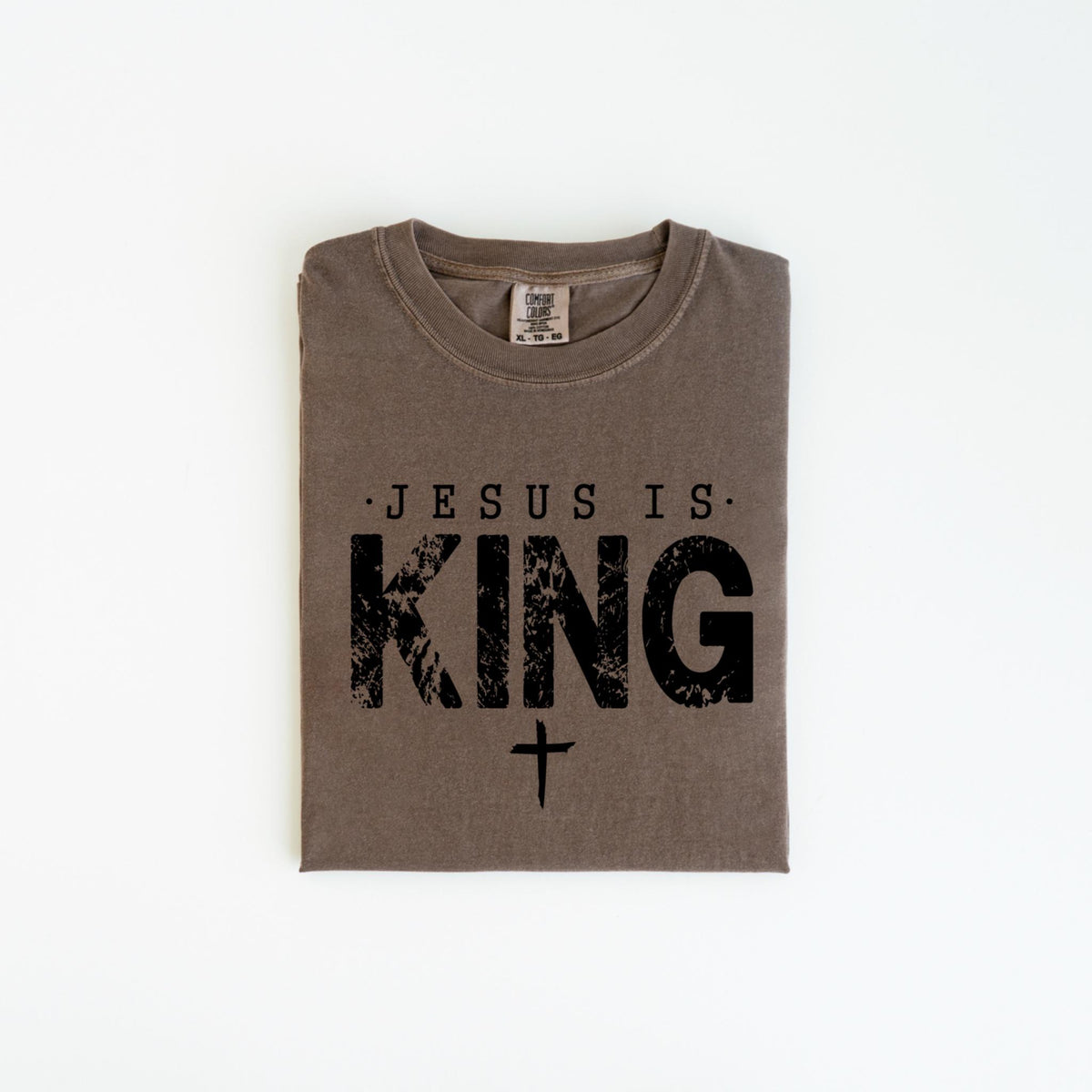 May include: A folded, brown t-shirt with the text "JESUS IS KING" in black, distressed lettering, and a small cross below. The shirt is made of a soft material and has a crew neck.