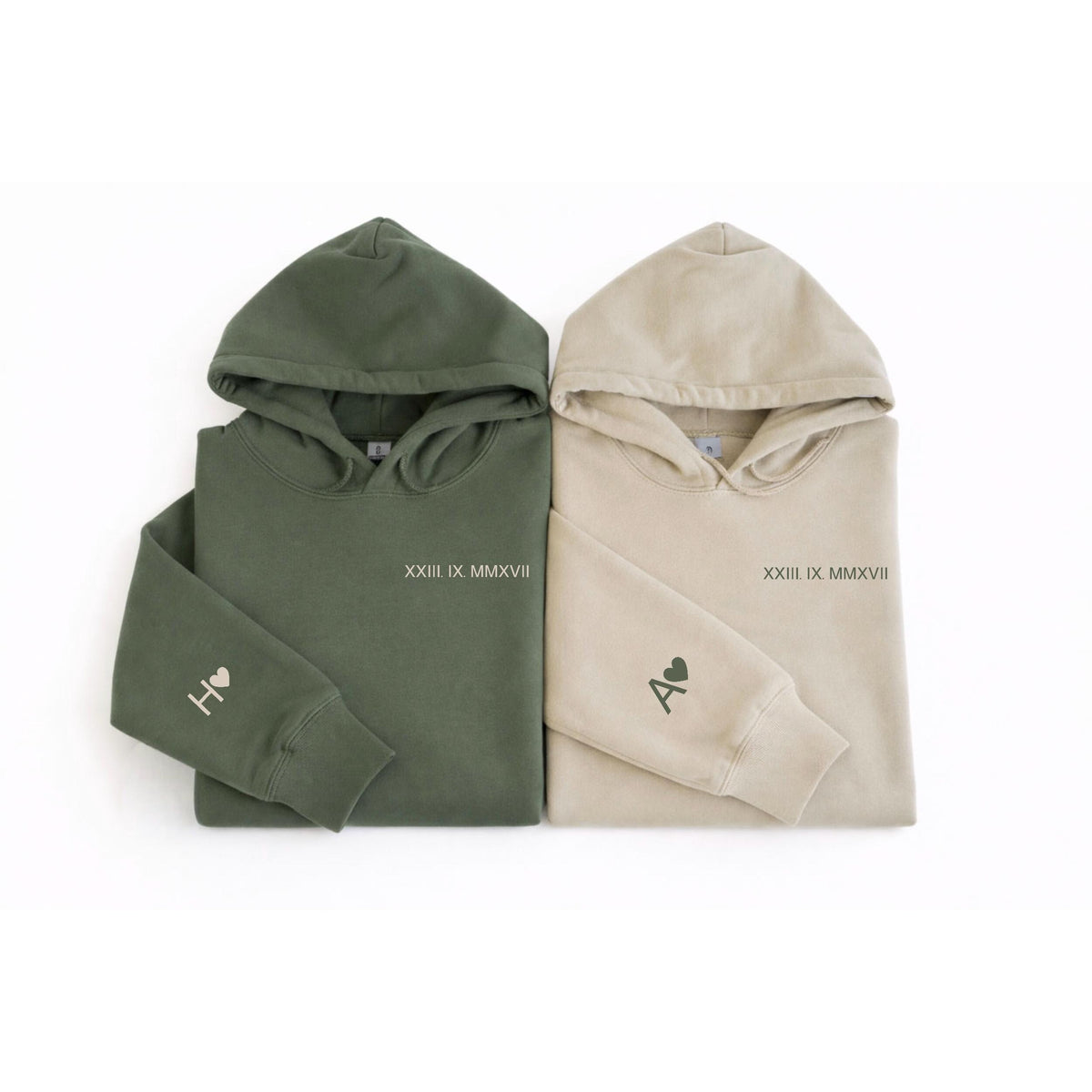 May include: Two hooded sweatshirts, one olive green and one beige. Each has a hood, long sleeves, and the Roman numeral date "XXIII IX MMXVII" printed on the chest. The left sleeve of each sweatshirt has a letter and a heart.