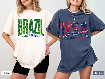 May include: Two oversized t-shirts, one ivory and one denim, are displayed. The ivory shirt features "BRAZIL" in green with a tropical design and "VAMOS BRASIL!" below. The denim shirt has "USA" in red, white, and blue with "ONE NATION UNDER GOD".