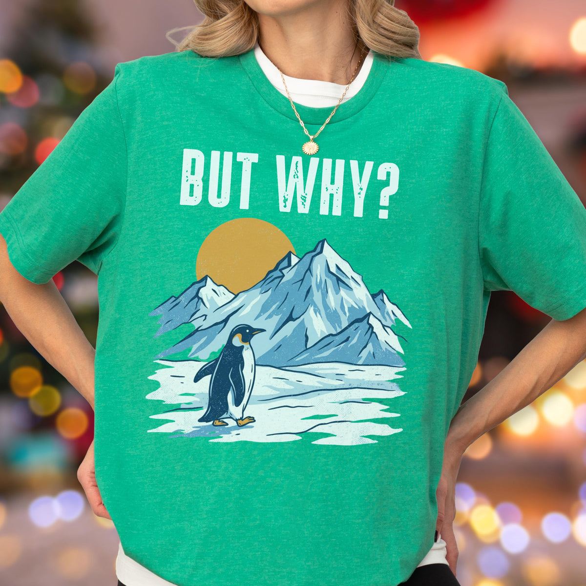 May include: Green t-shirt with the phrase "BUT WHY?" in white block letters. The shirt features a graphic of a penguin standing in front of snow-capped mountains and a yellow sun. The penguin is black and white.