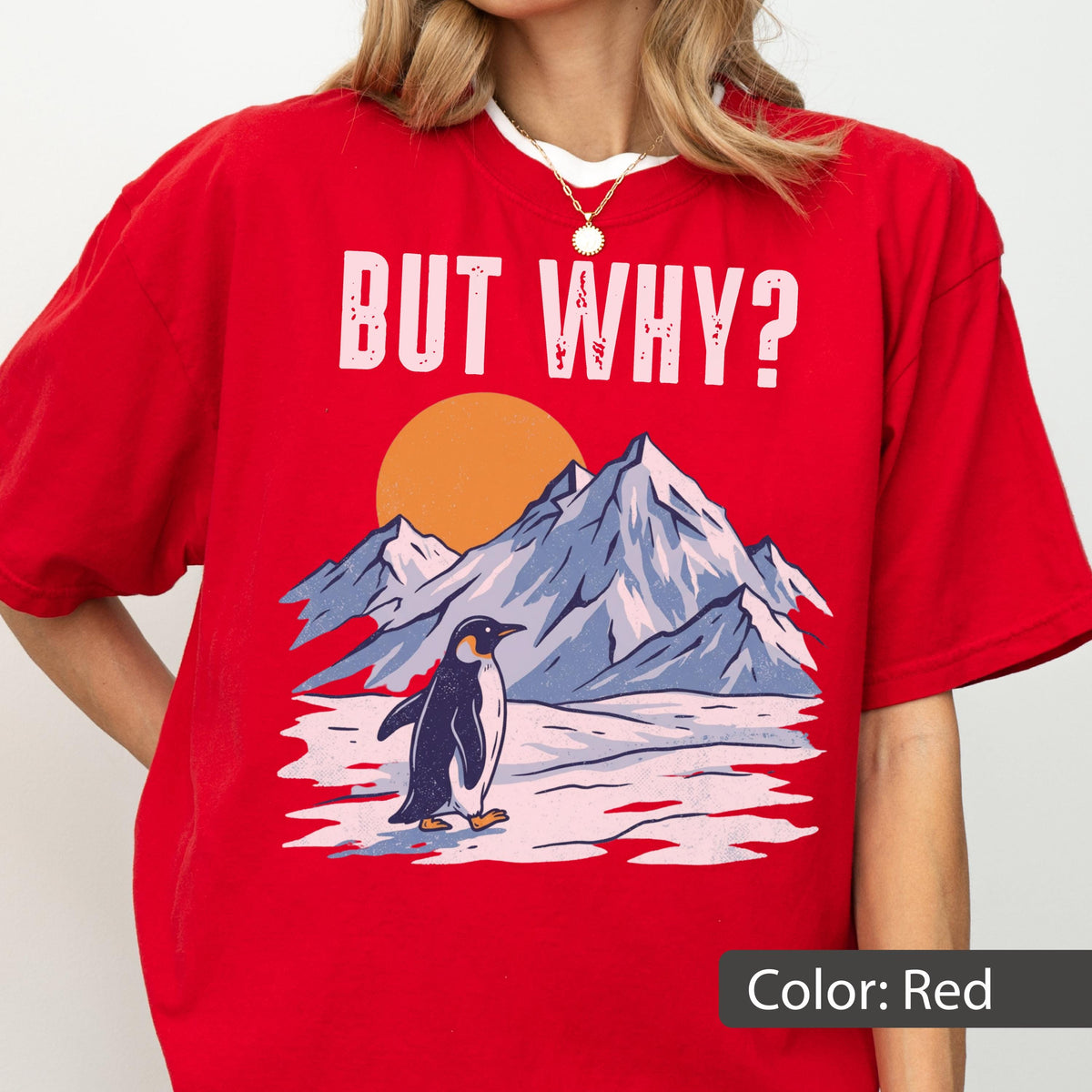 May include: Red t-shirt with a graphic of a penguin standing in front of mountains and a setting sun. The text "BUT WHY?" is printed above the graphic. The shirt is a solid red color.