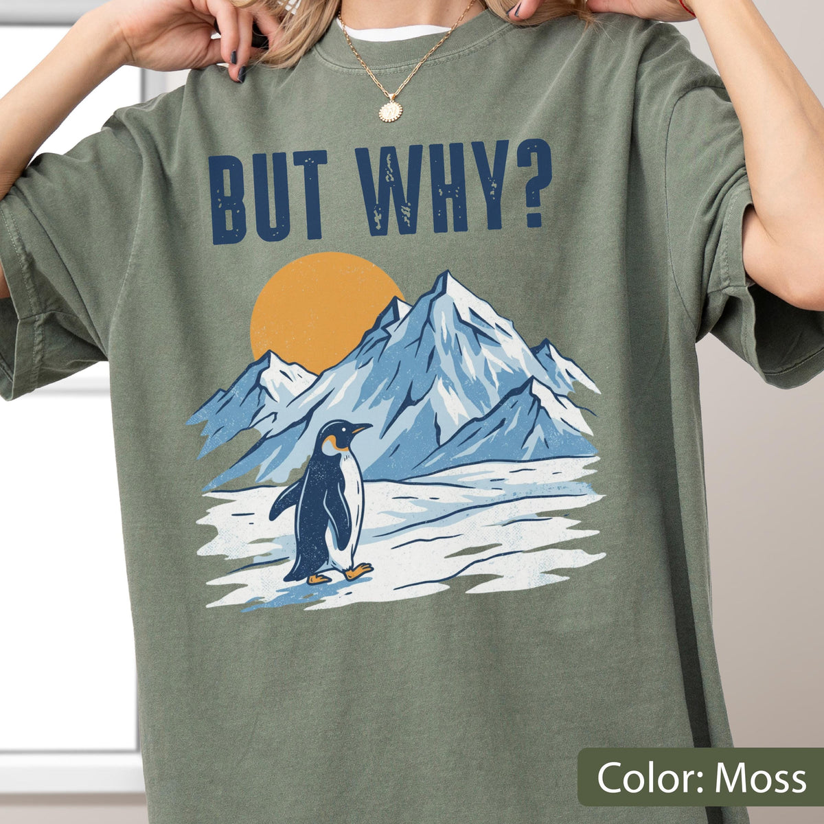 May include: Moss green t-shirt with the text "BUT WHY?" above a graphic of a penguin, mountains, and a sun. The penguin is black and white, and the mountains are blue and white.