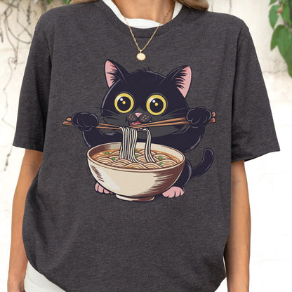 May include: Dark gray t-shirt featuring a cartoon black cat holding chopsticks with noodles over a bowl of soup. The cat has large yellow eyes and pink ears and paws. The shirt has a white collar.
