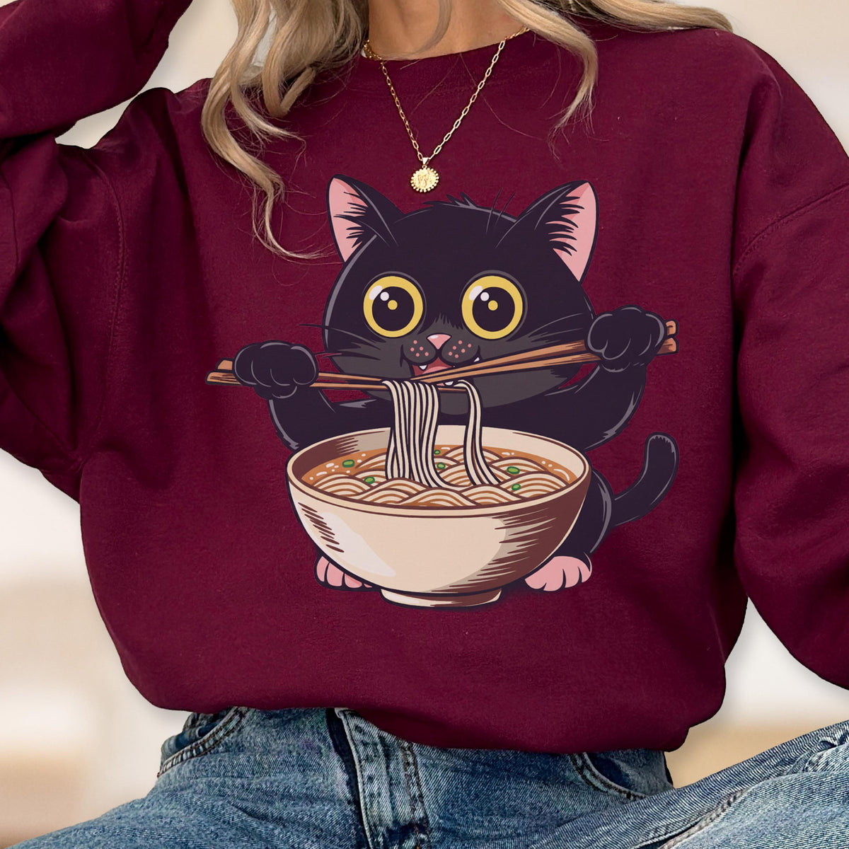 May include: Burgundy sweatshirt featuring a cartoon black cat eating ramen noodles with chopsticks. The cat has large yellow eyes and pink ears and paws. The ramen bowl is beige with brown noodles and green toppings. The sweatshirt is a solid burgundy color.