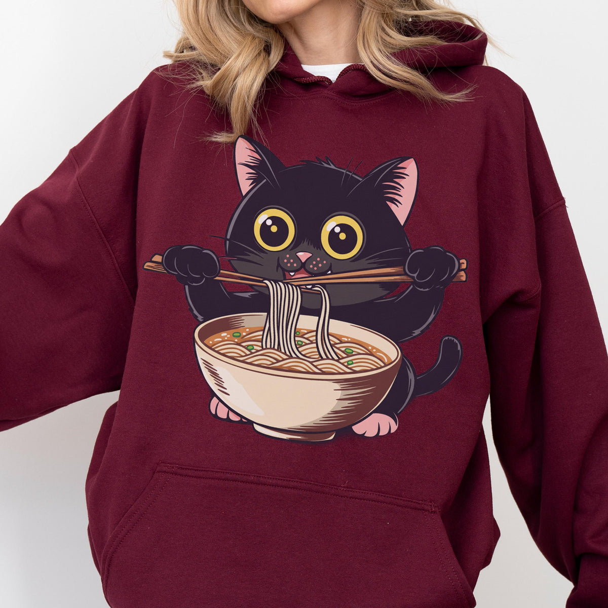 May include: Burgundy hoodie featuring a cartoon black cat with large yellow eyes, holding chopsticks and eating noodles from a bowl. The cat is the central focus, with the ramen bowl below. The hoodie is a solid burgundy color.
