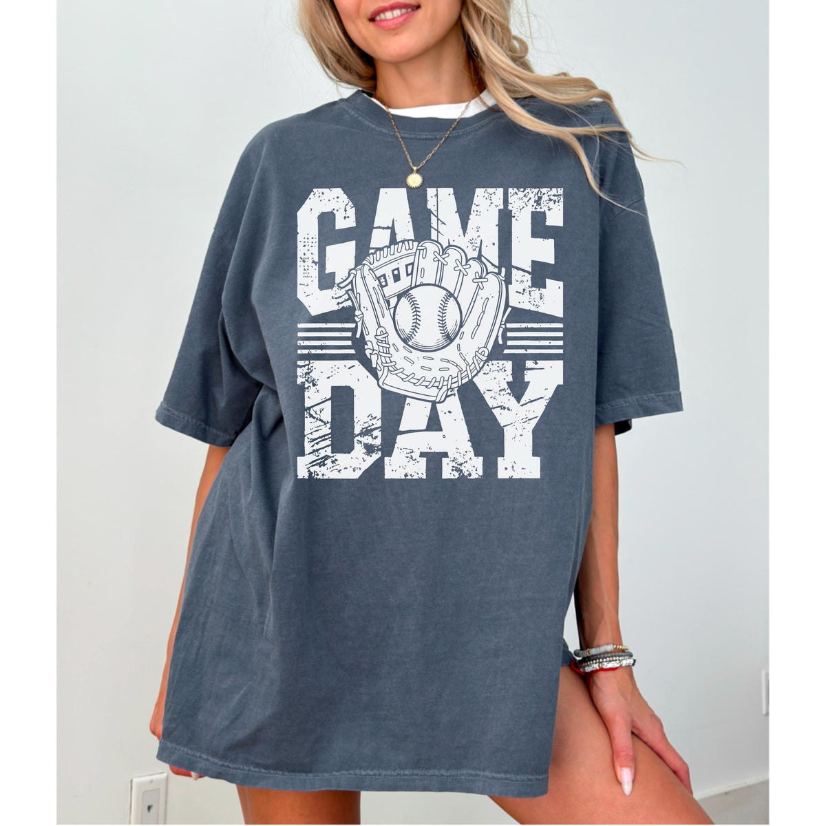 May include: Dark grey t-shirt with the words "GAME DAY" in white block letters. A baseball and glove graphic is centered on the shirt. The shirt has short sleeves and a relaxed fit.