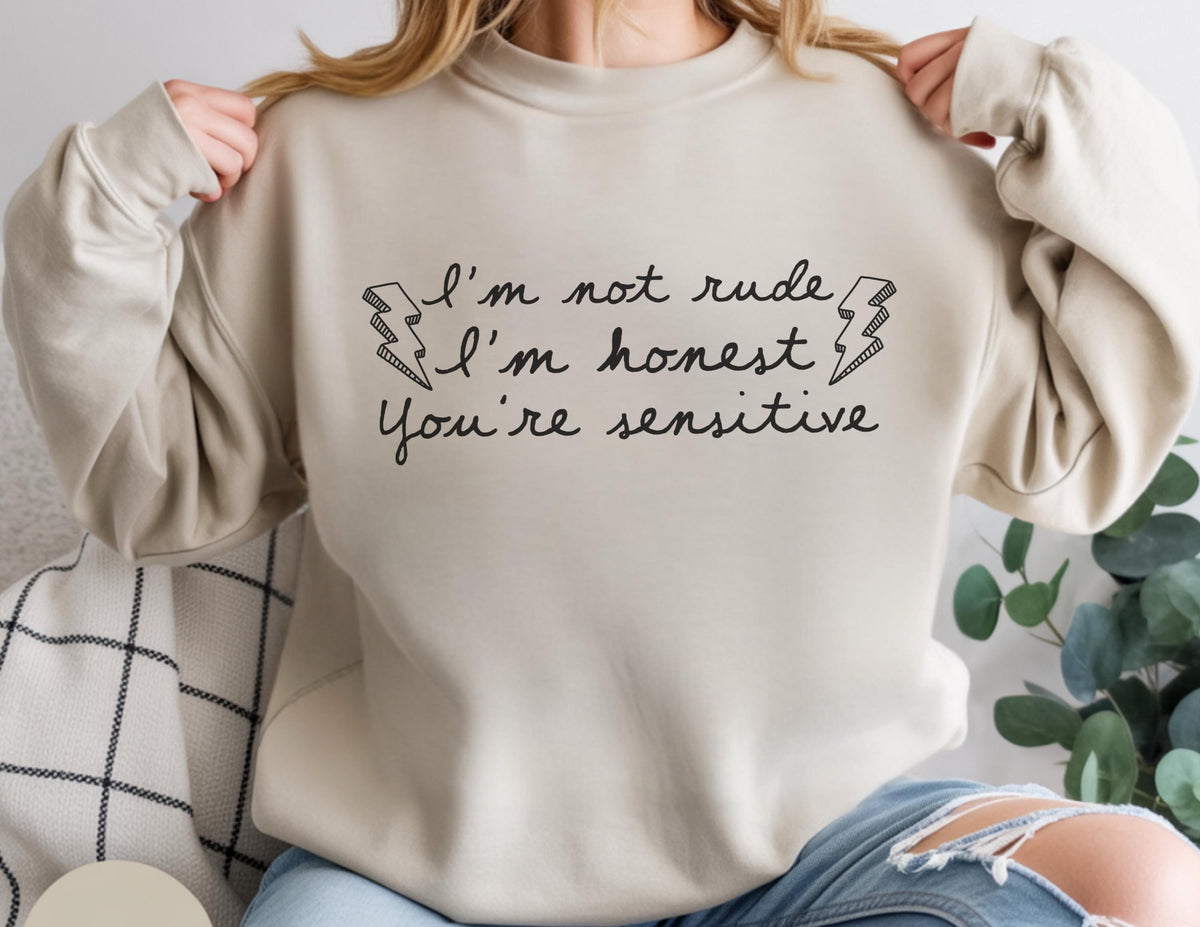 May include: Beige sweatshirt with the text "I'm not rude, I'm honest, You're sensitive" in black script. The design includes two lightning bolt graphics. The sweatshirt is a crew neck style.