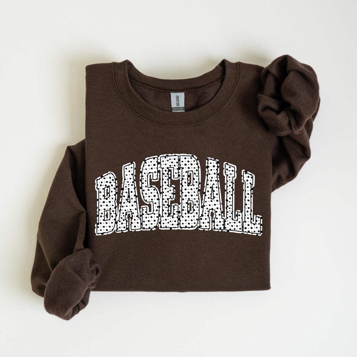 May include: A brown sweatshirt with the word "BASEBALL" in large, white, dotted letters across the front. The sweatshirt has long sleeves and a crew neck. The sleeves are folded up.