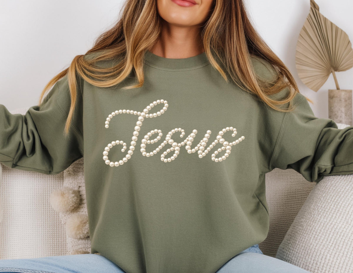 May include: Olive green sweatshirt with the word "Jesus" spelled out in a cursive font using faux pearls. The sweatshirt has a crew neck and long sleeves. The design is centered on the front of the garment.