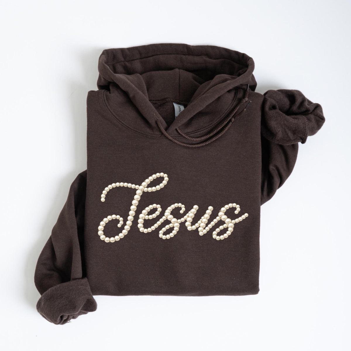 May include: A dark brown hoodie with the word "Jesus" spelled out in off-white faux pearls. The hoodie has a drawstring hood and long sleeves. The garment is folded neatly on a white surface.