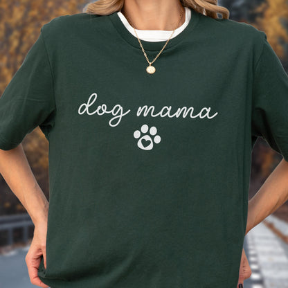 May include: Dark green t-shirt with the words "dog mama" in cursive script and a white paw print graphic. The shirt has a white crew neck collar and is worn with a gold necklace.