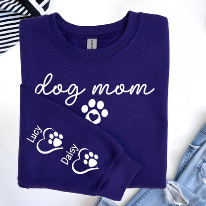 May include: A dark purple sweatshirt with the words "dog mom" in white script, along with a paw print with a heart. The sleeve features the names "Lucy" and "Daisy" with paw prints inside hearts. The sweatshirt is made of a soft material.