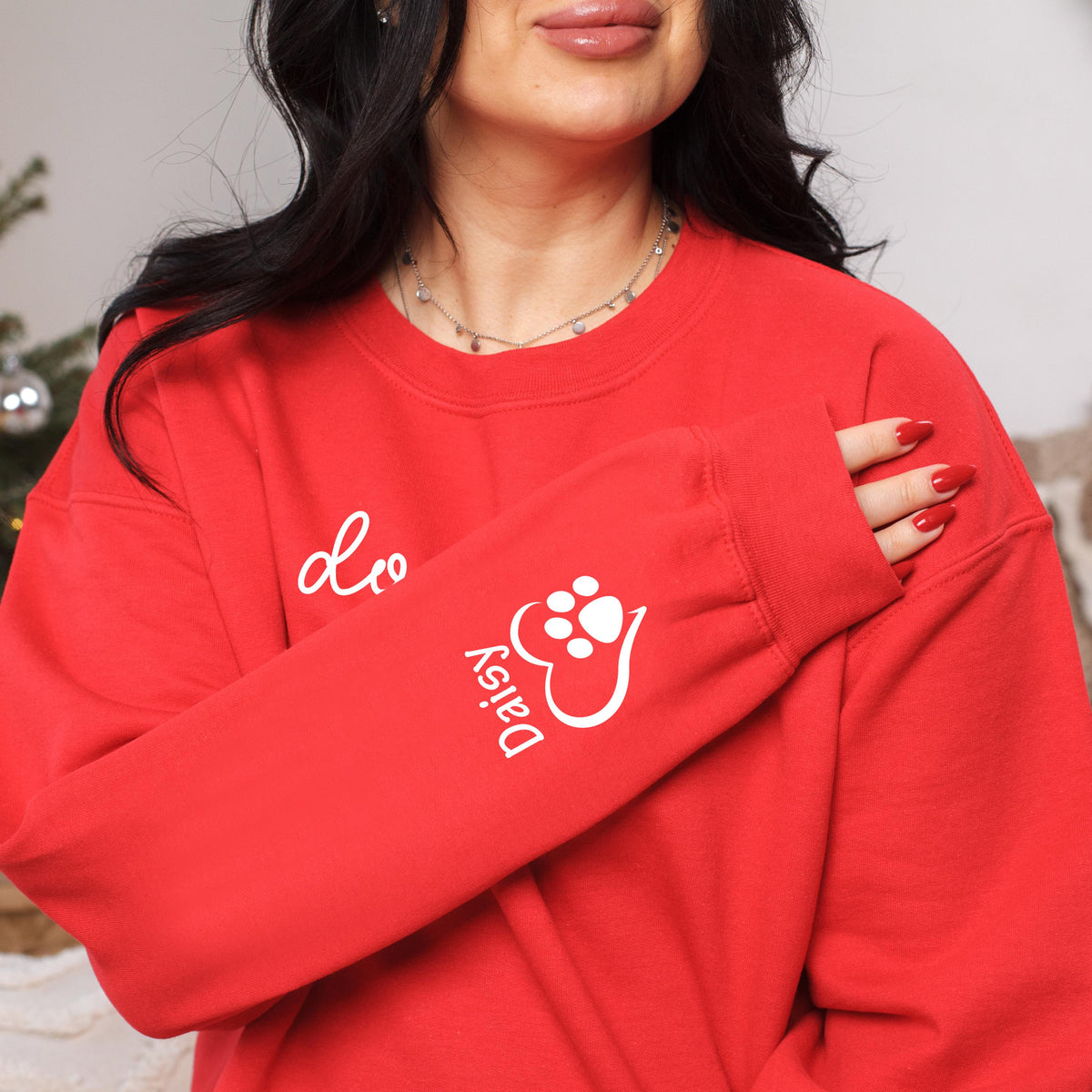 May include: A red sweatshirt with white text and a paw print design. The sleeve features the name "Daisy" and a paw print inside a heart. The word "Leo" is written on the chest. The sweatshirt is a casual style.