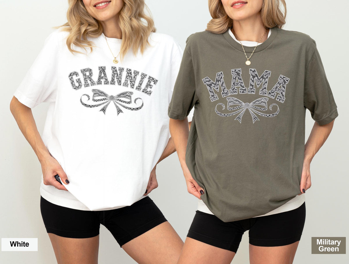 May include: Two short-sleeved t-shirts, one white and one military green. The white shirt has the word "GRANNIE" above a bow design. The green shirt has the word "MAMA" above a bow design. Both designs are in a black and white pattern.