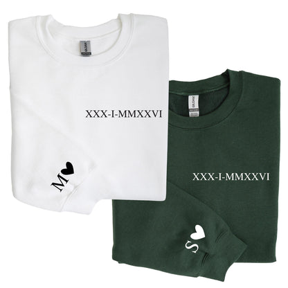 May include: A white sweatshirt with black text reading XXX-I-MMXXVI and a black letter M with a heart on the sleeve, alongside a dark green sweatshirt with white text reading XXX-I-MMXXVI and a white letter S with a heart on the sleeve.