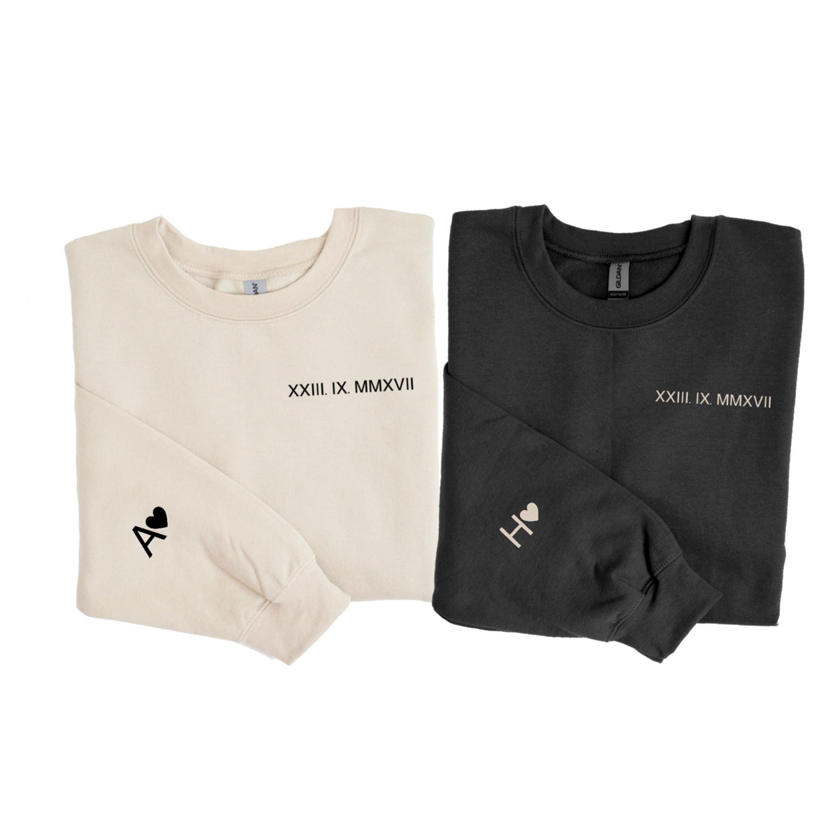 May include: Two long-sleeved sweatshirts, one cream and one black. Each has a date in Roman numerals and a letter with a heart on the sleeve. The cream sweatshirt has the letter "A" and the black sweatshirt has the letter "H".