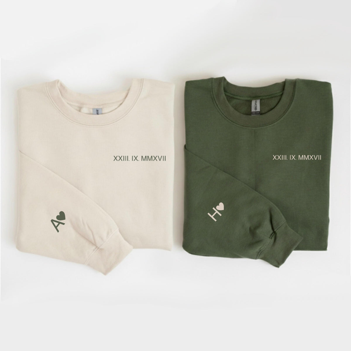 May include: Two long-sleeved sweatshirts, one cream and one olive green. Each has a date in Roman numerals and a letter with a heart on the sleeve. The cream sweatshirt has the letter "A" and the olive green sweatshirt has the letter "H".