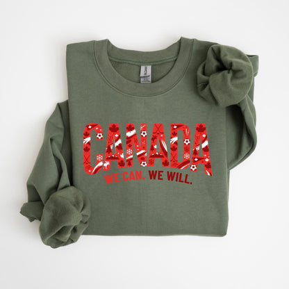 May include: An olive green sweatshirt with the word "CANADA" in large red letters filled with maple leaves, hockey sticks, and snowflakes. Below the word "CANADA" is the phrase "WE CAN. WE WILL."
