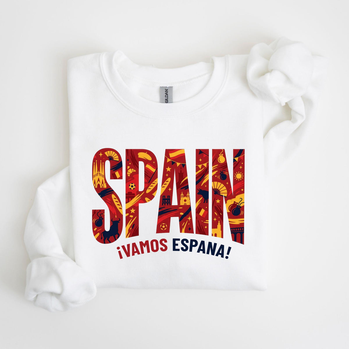 May include: White sweatshirt with the word "SPAIN" in large, red, yellow, and blue letters. The letters are filled with Spanish-themed illustrations. Below the word "SPAIN" is the phrase "¡VAMOS ESPAÑA!" in red and yellow.