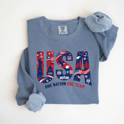 May include: A blue crew neck sweatshirt with the word "USA" in red, white, and blue, featuring iconic American imagery. The text "ONE NATION ONE TEAM" is below the word "USA".