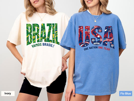 May include: Two oversized t-shirts. One is ivory with "BRAZIL" in green and yellow, and "VAMOS BRASIL!" below. The other is blue with "USA" in red and blue, with "ONE NATION ONE TEAM" below. Both shirts have short sleeves.