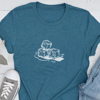 May include: Teal t-shirt featuring a white graphic of three ice cubes melting. The design is a simple, line-art style. The shirt has a crew neck and short sleeves. A pair of gray sneakers and blue jeans are visible in the image.