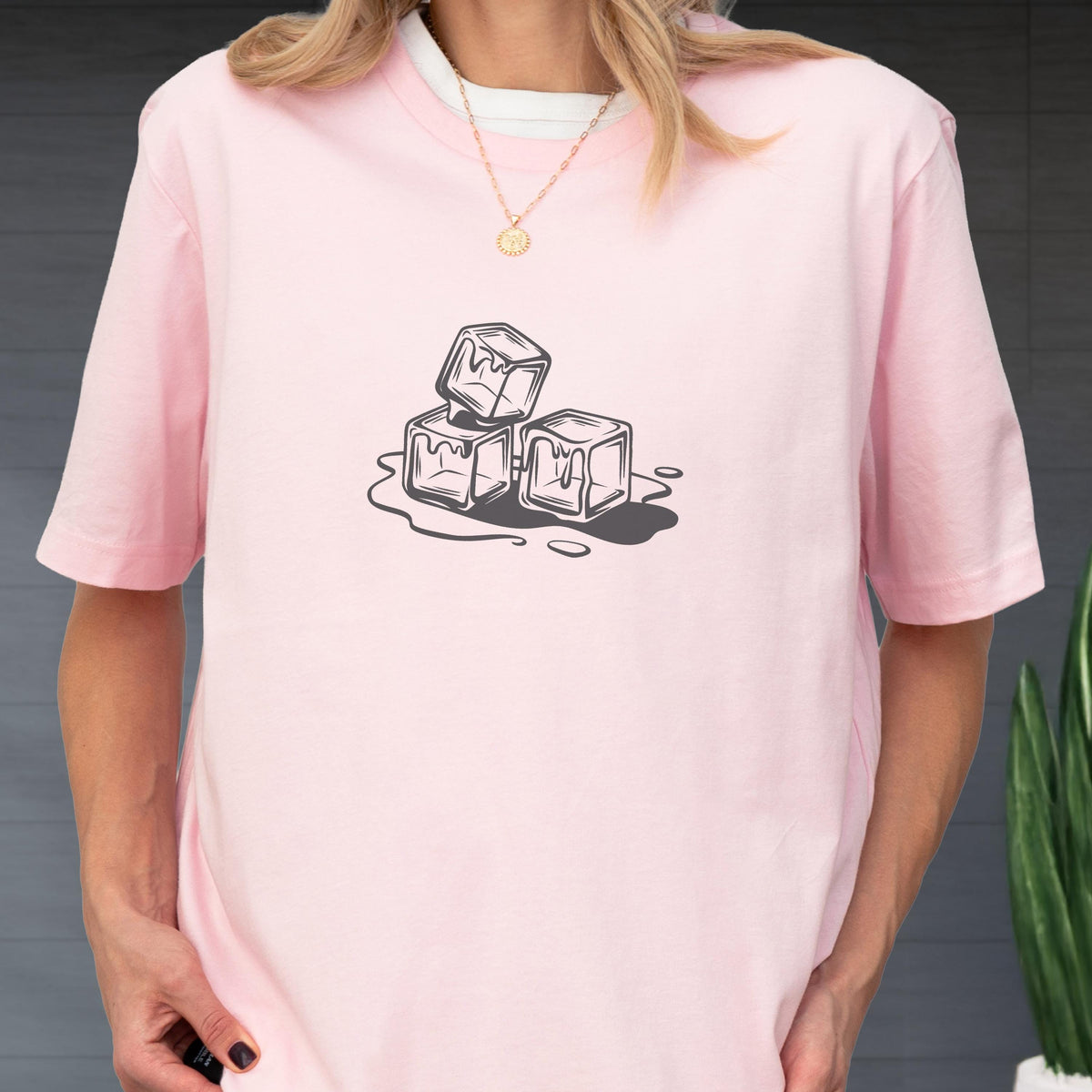 May include: A light pink t-shirt featuring a black and white graphic of three melting ice cubes. The shirt has short sleeves and a crew neck. The design is centered on the front of the shirt.