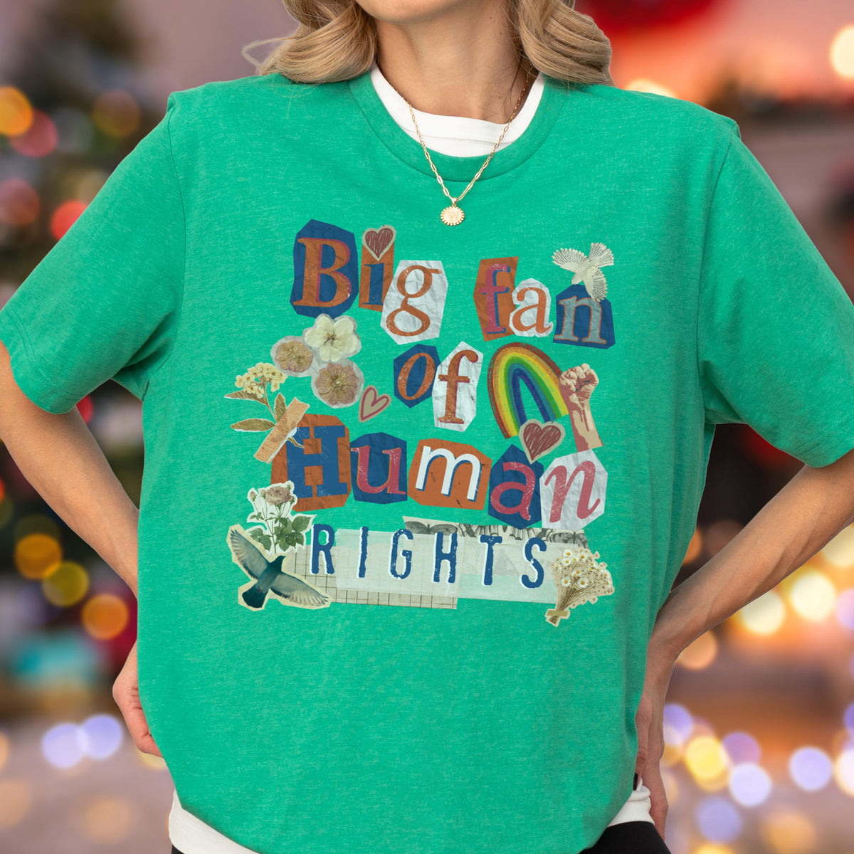 May include: Green t-shirt with the text "Big fan of Human Rights" in a collage style. The design includes a rainbow, flowers, and a raised fist. The shirt has short sleeves and a crew neck.