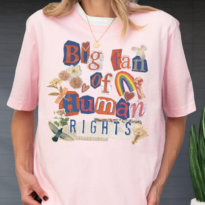 May include: Pink short-sleeved t-shirt with the text "Big fan of Human Rights" in a collage style. The design includes a rainbow, hearts, and floral elements. The shirt has a white crew neck collar.