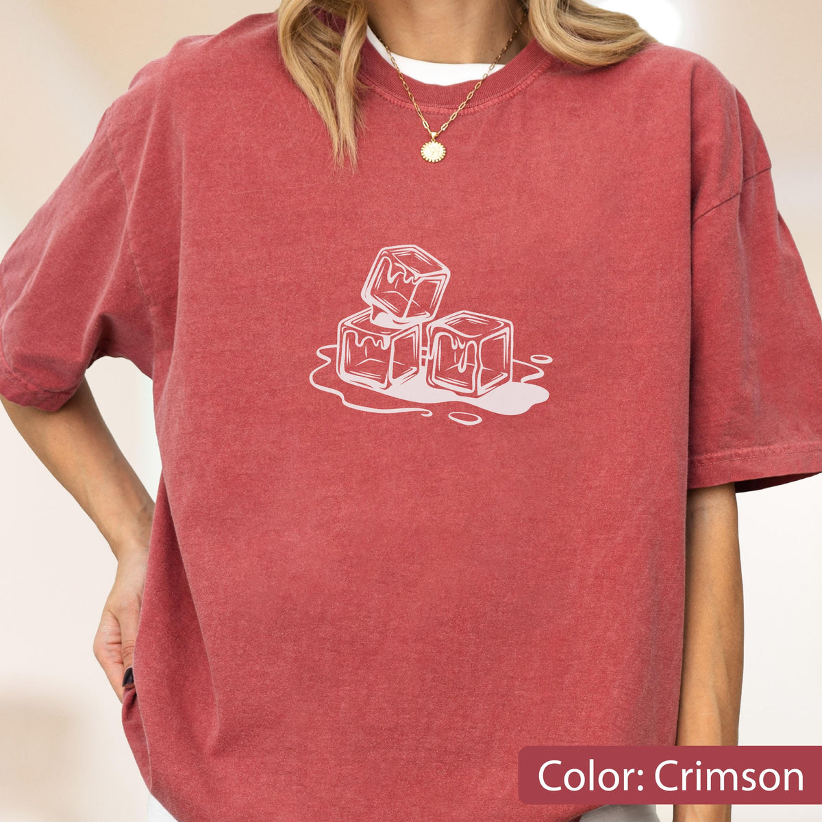 May include: Crimson-colored t-shirt featuring a white graphic of melting ice cubes. The shirt has short sleeves and a crew neck. The text "Color: Crimson" is at the bottom of the image. The shirt is made of a soft material.