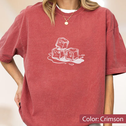 May include: Crimson-colored t-shirt featuring a white graphic of melting ice cubes. The shirt has short sleeves and a crew neck. The text "Color: Crimson" is at the bottom of the image. The shirt is made of a soft material.