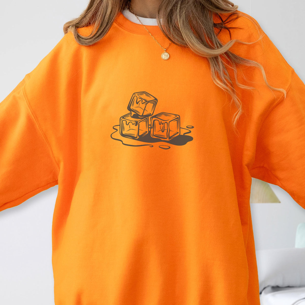 May include: Bright orange sweatshirt featuring a graphic of three melting ice cubes. The design is in a dark brown color. The sweatshirt is a solid, vibrant orange color.